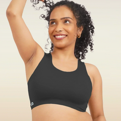 Woman wearing a black sports bra and pink underwear against a beige background
