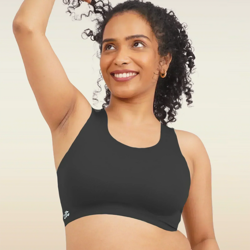 Woman wearing a black sports bra and pink underwear against a beige background