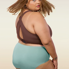Woman wearing a brown bikini top and blue mid-waist underwear on a beige background