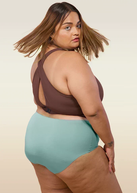 Woman wearing a brown bikini top and blue mid-waist underwear on a beige background