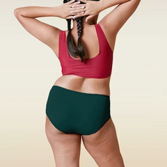 Person wearing a red sports bra and teal mid-waist underwear on a beige background
