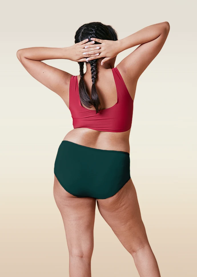Person wearing a red sports bra and teal mid-waist underwear on a beige background