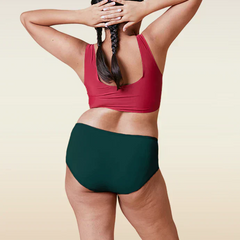 Person wearing a red sports bra and teal mid-waist underwear on a beige background