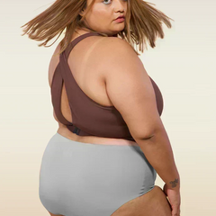 Woman wearing a brown cross-back sports bra and gray mid-waist underwear on a beige background