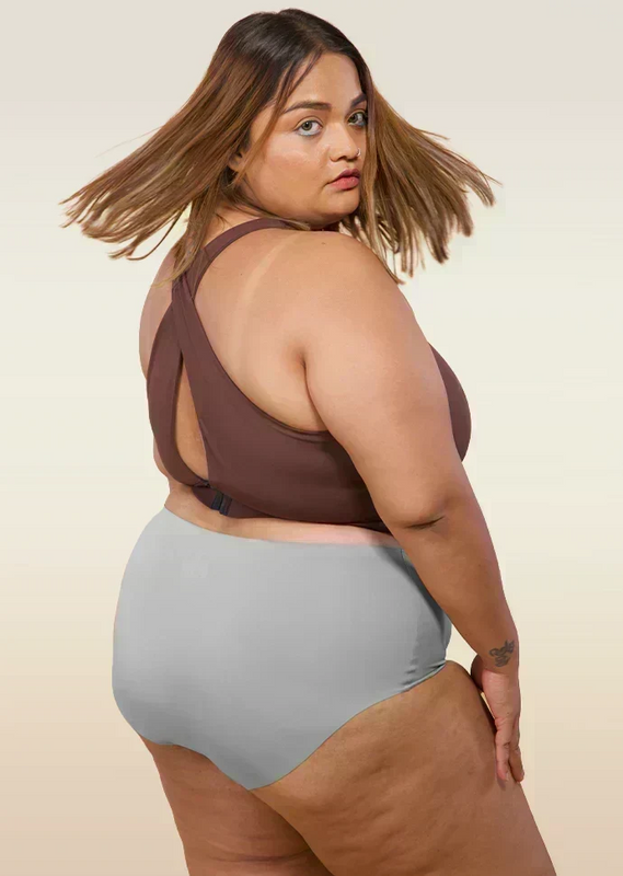 Woman wearing a brown cross-back sports bra and gray mid-waist underwear on a beige background