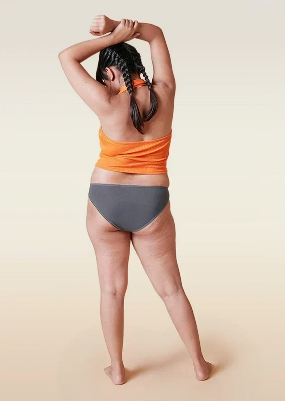 Person wearing an orange top and gray underwear on a beige background