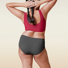 Person wearing a red sports bra and gray mid-waist underwear on a beige background