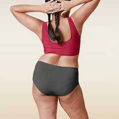 Person wearing a red sports bra and gray mid-waist underwear on a beige background