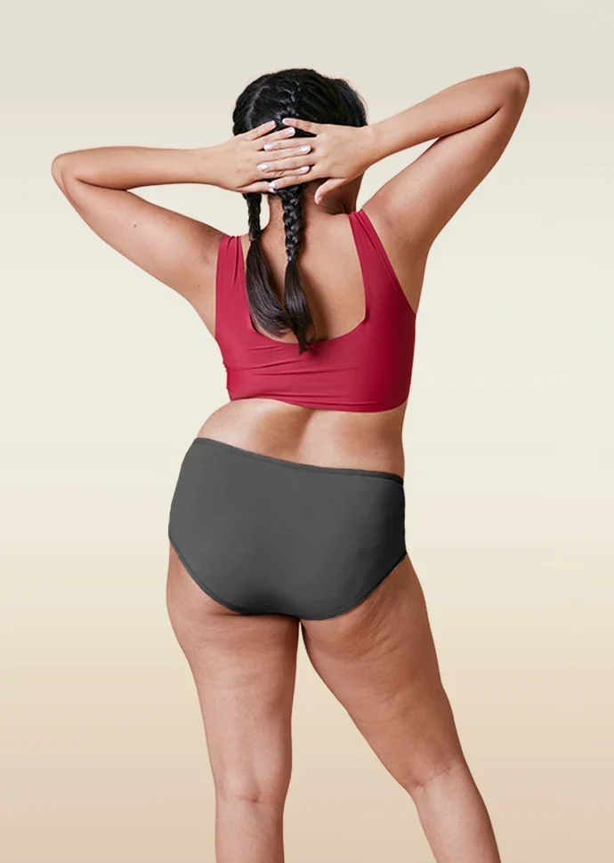 Person wearing a red sports bra and gray mid-waist underwear on a beige background