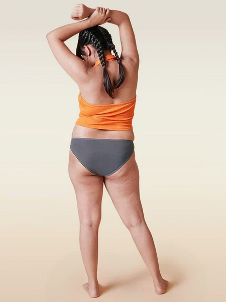 Person wearing an orange top and gray underwear on a beige background