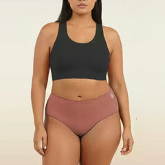 Woman wearing a black sports bra and pink mid-waist underwear on a beige background