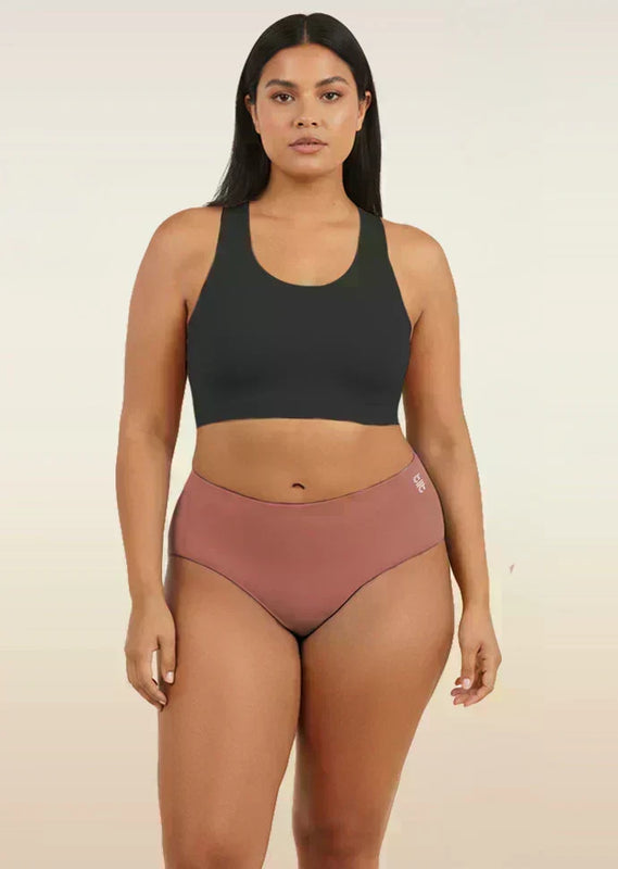 Woman wearing a black sports bra and pink mid-waist underwear on a beige background