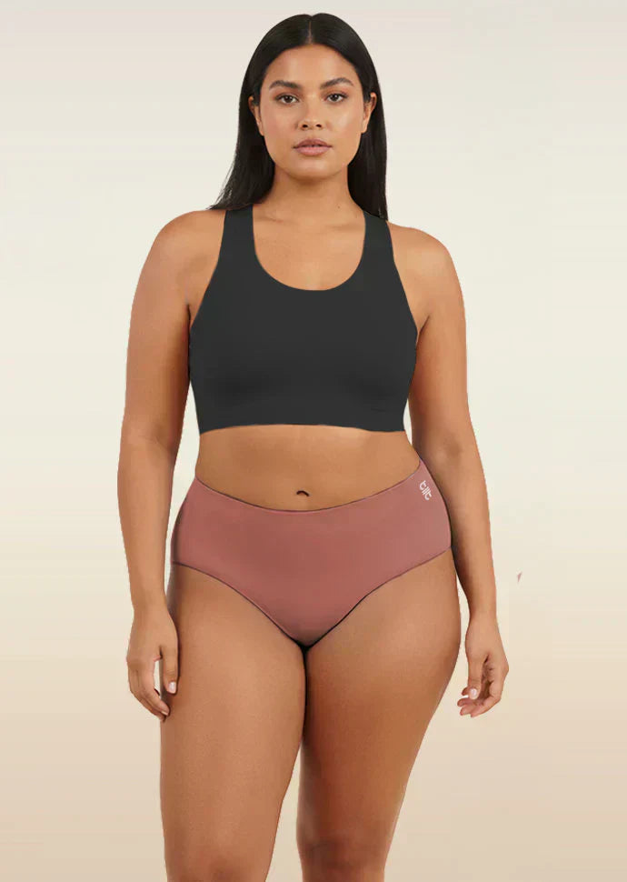 Woman wearing a black sports bra and pink mid-waist underwear on a beige background