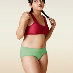 Woman wearing a red sports bra and green shorts against a beige background