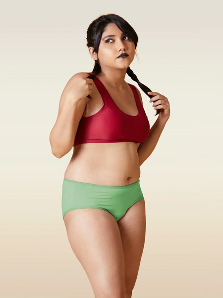 Woman wearing a red sports bra and green shorts against a beige background