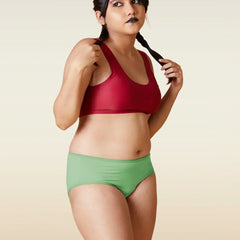 Woman wearing a red sports bra and green shorts against a beige background