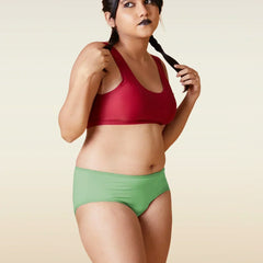 Woman wearing a red sports bra and green shorts against a beige background