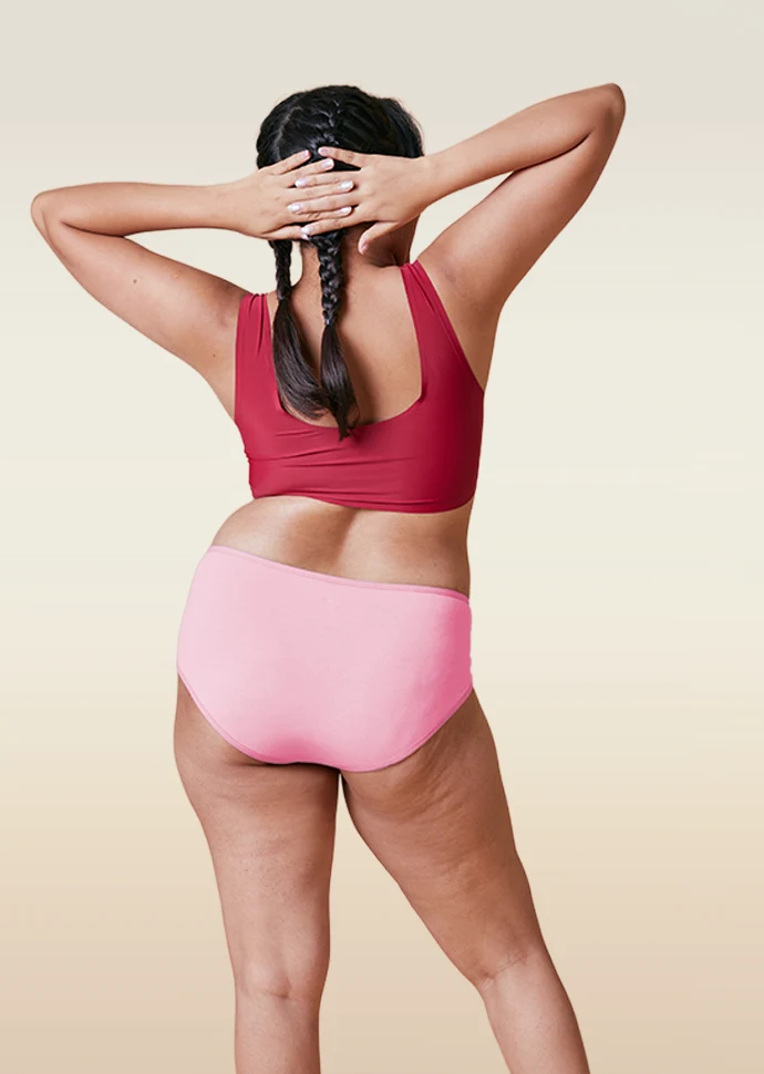 Person wearing a red sports bra and pink mid-waist underwear on a beige background