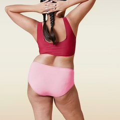 Person wearing a red sports bra and pink mid-waist underwear on a beige background