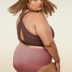 Woman wearing a brown sports bra and mid-waist pink underwear on a beige background