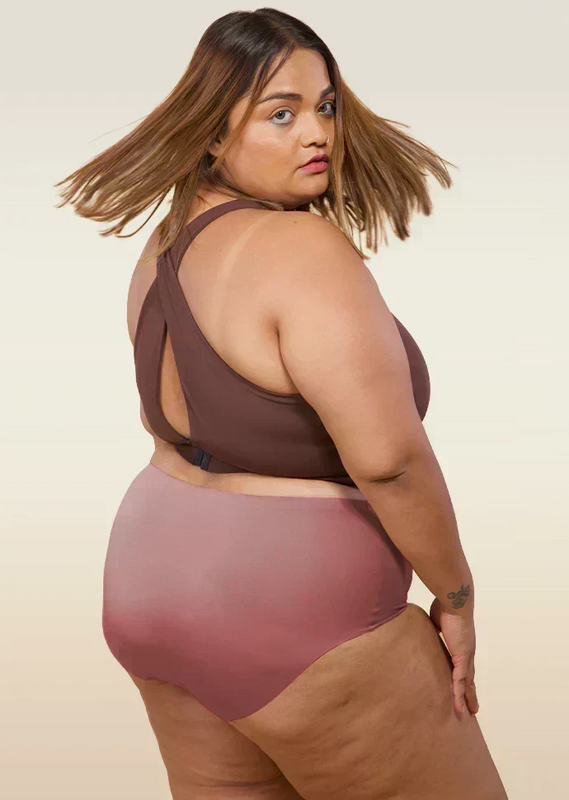 Woman wearing a brown sports bra and mid-waist pink underwear on a beige background