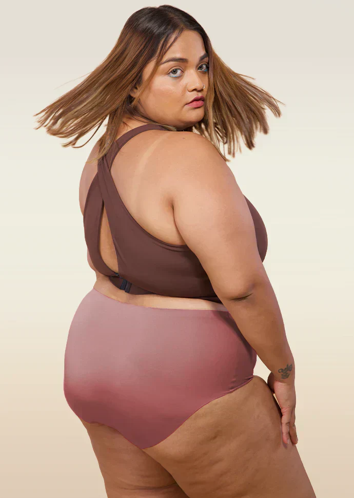 Woman wearing a brown sports bra and mid-waist pink underwear on a beige background