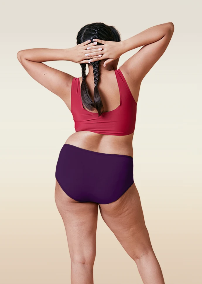 Person wearing a red sports bra and  violet mid-waist underwear on a beige background